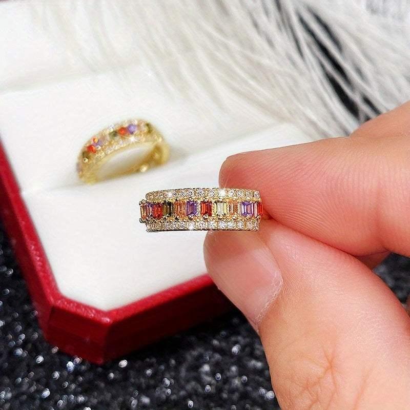 Rainbow gemstone eternity ring with diamond accents, held near red gift box